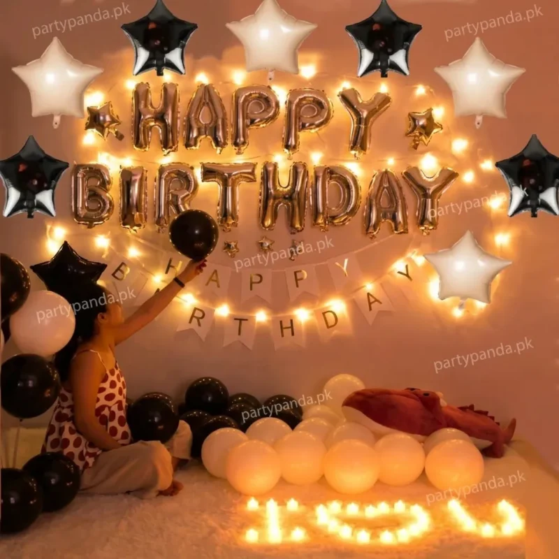 Black and gold theme birthday balloon decoration set with star foil balloons, fairy lights, and happy birthday banner by PartyPanda.pk